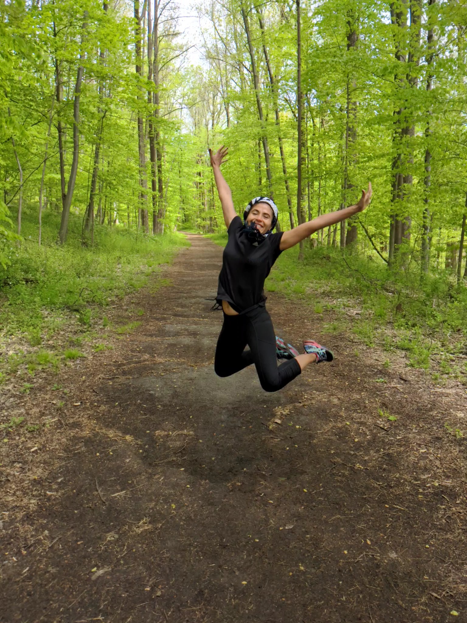 Lady with a smile jumping off the ground on a forest trail